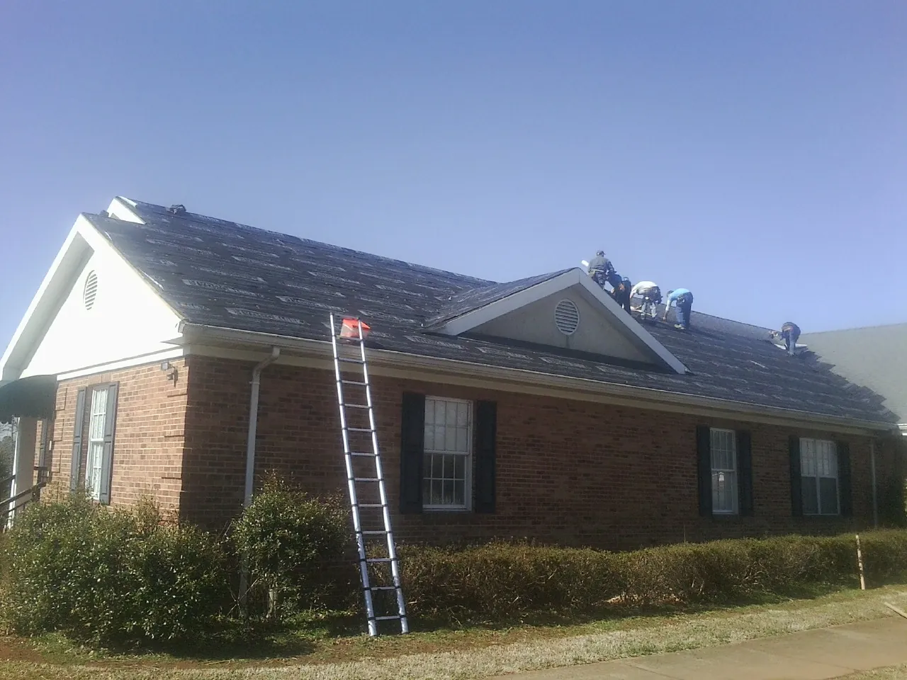 Crew tearing shingles off a brick ranch roof with a ladder set — Metal Roof Repair work by our crew in Reedsport