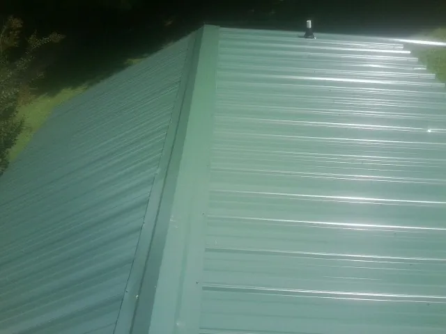 New green metal panels meeting at the ridge of a roof — Flat Roof Repair work by our crew in Reedsport