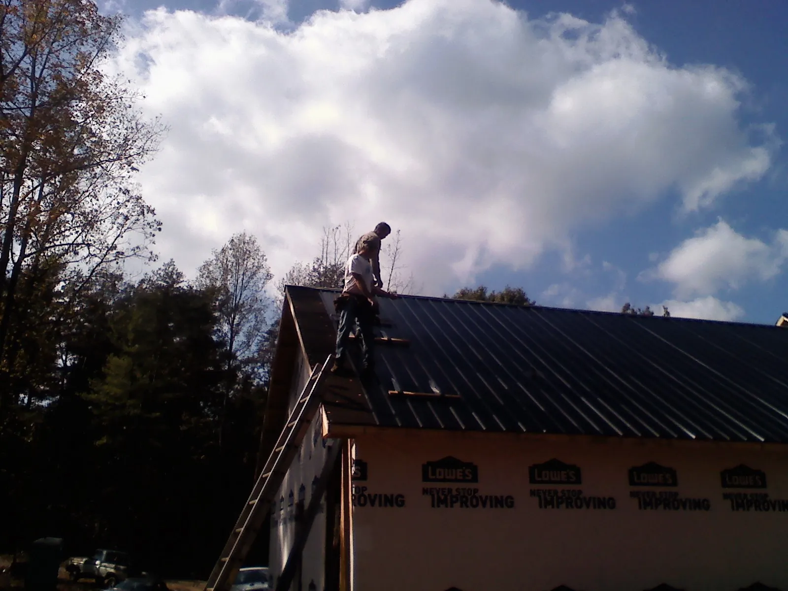 Roofer fastening dark metal panels high against a cloudy sky, from a Roof Inspection job in Reedsport