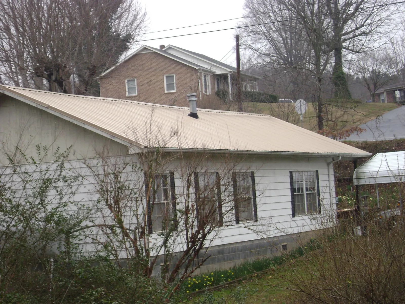 Tan metal roof on a white sided house set into a hillside — Commercial Roofing by Roofing Brothers in Reedsport